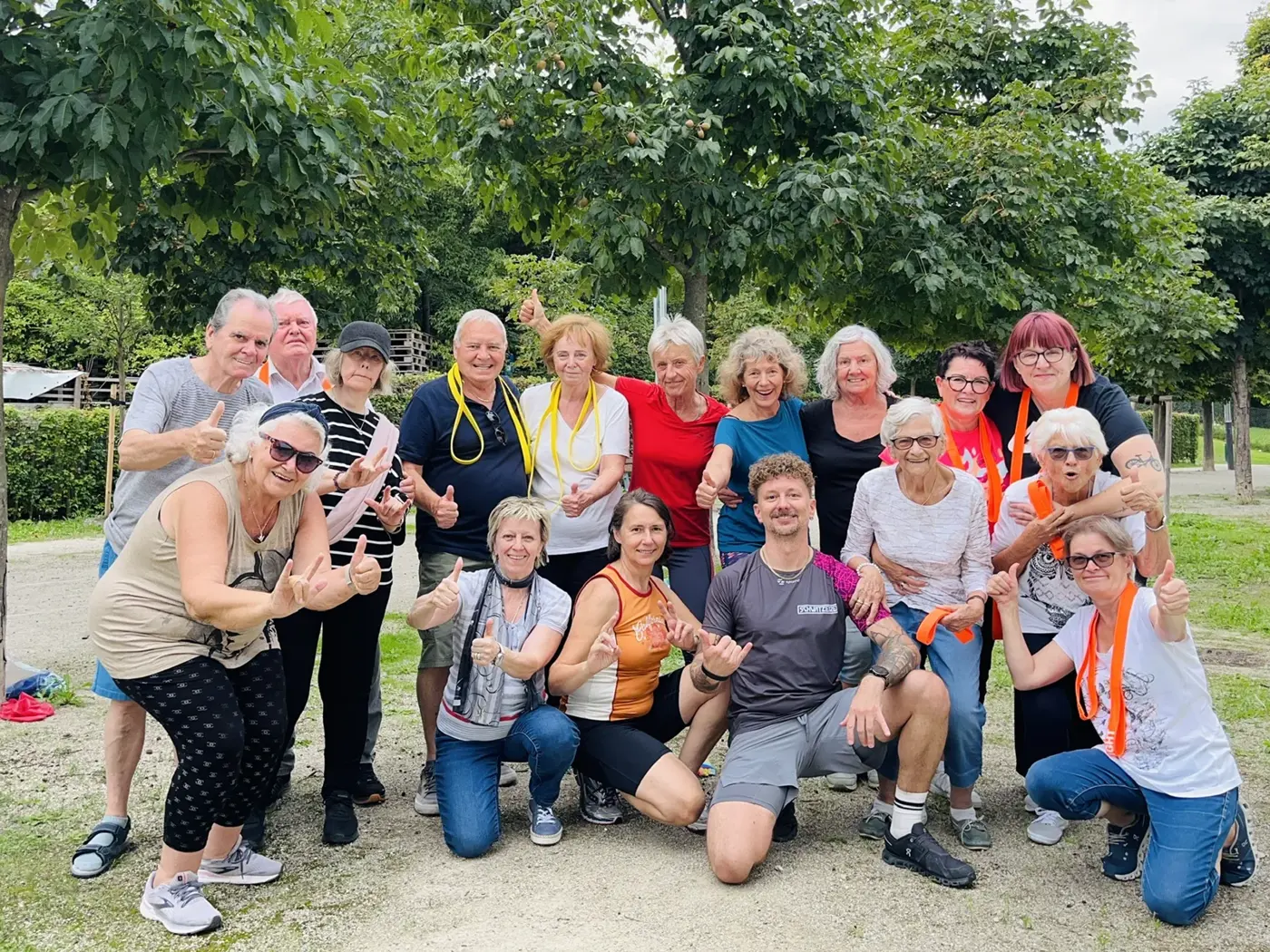 Eine große Gruppe von älteren Frauen und Männern lacht in die Kamera. Viele zeigen den Daumen nach oben. Vorne kniet Trainer Manfred.