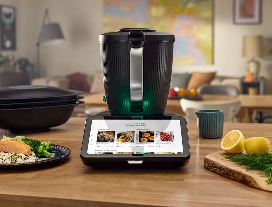 Thermomix TM7 auf einem Holztisch, daneben Lachs mit Brokkoli und Reis